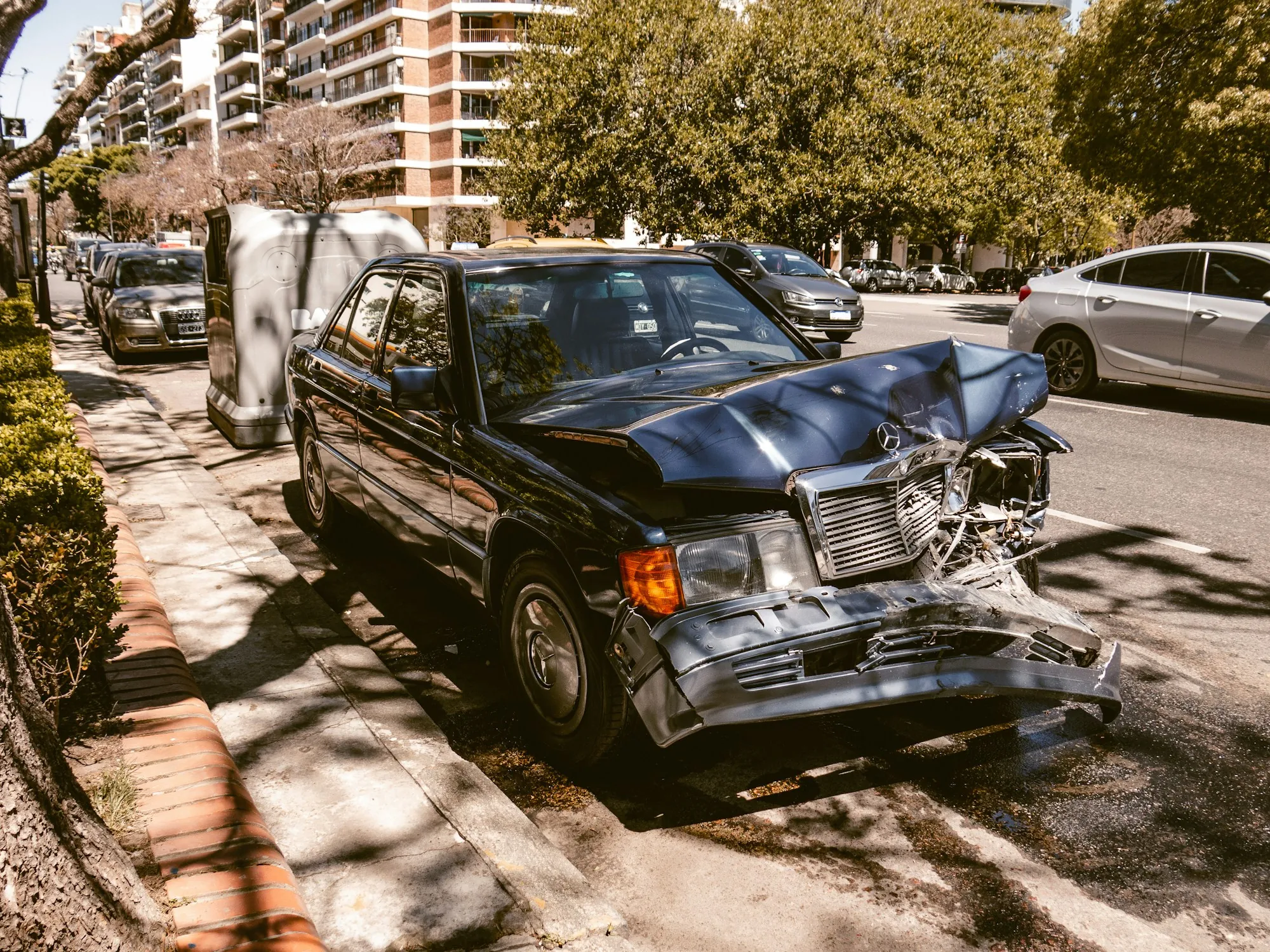 Dark sedan with a crushed front end parked on a city street